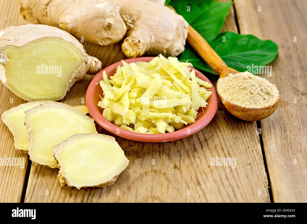Piatto di colore marrone con lo zenzero grattugiato, un cucchiaio di legno con polvere di radice di zenzero, foglie verdi sul pannello di legno Foto Stock