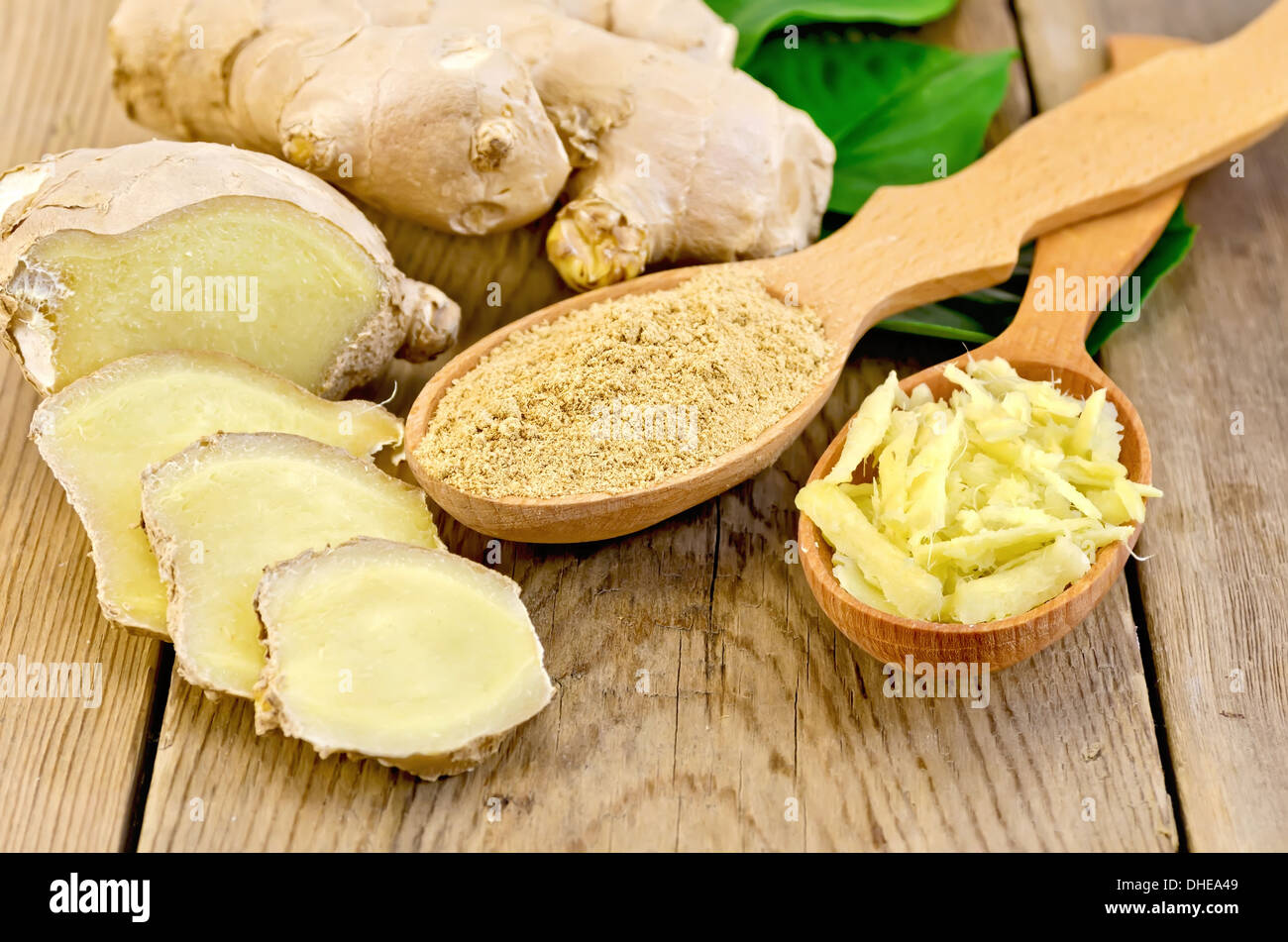 Grattugiato e lo zenzero in polvere in due cucchiai di legno, radice di zenzero, foglie verdi sul pannello di legno Foto Stock