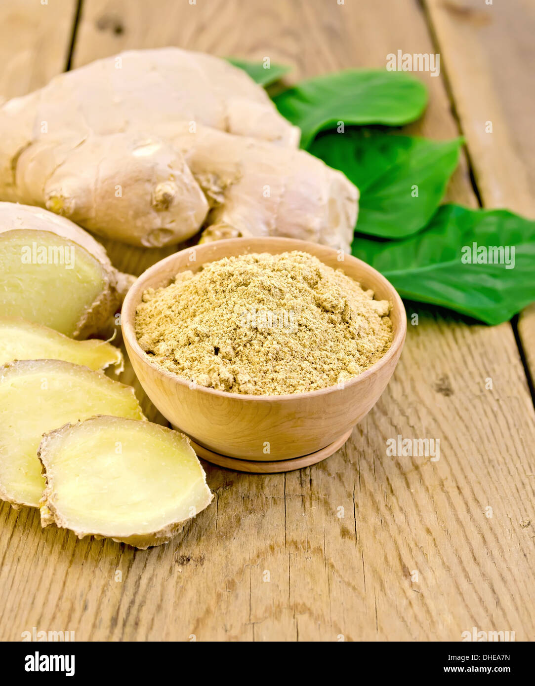 Lo zenzero in polvere in un recipiente di radice di zenzero, foglie verdi sullo sfondo del pannello di legno Foto Stock
