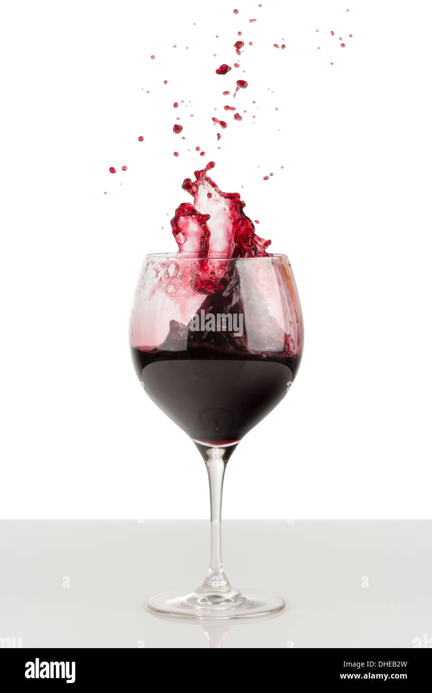 Spruzzata di vino rosso in vetro. Nelle vicinanze ci sono splatter di vino. Un vetro sorge su una lucida superficie grigia e isolato su bianco Foto Stock