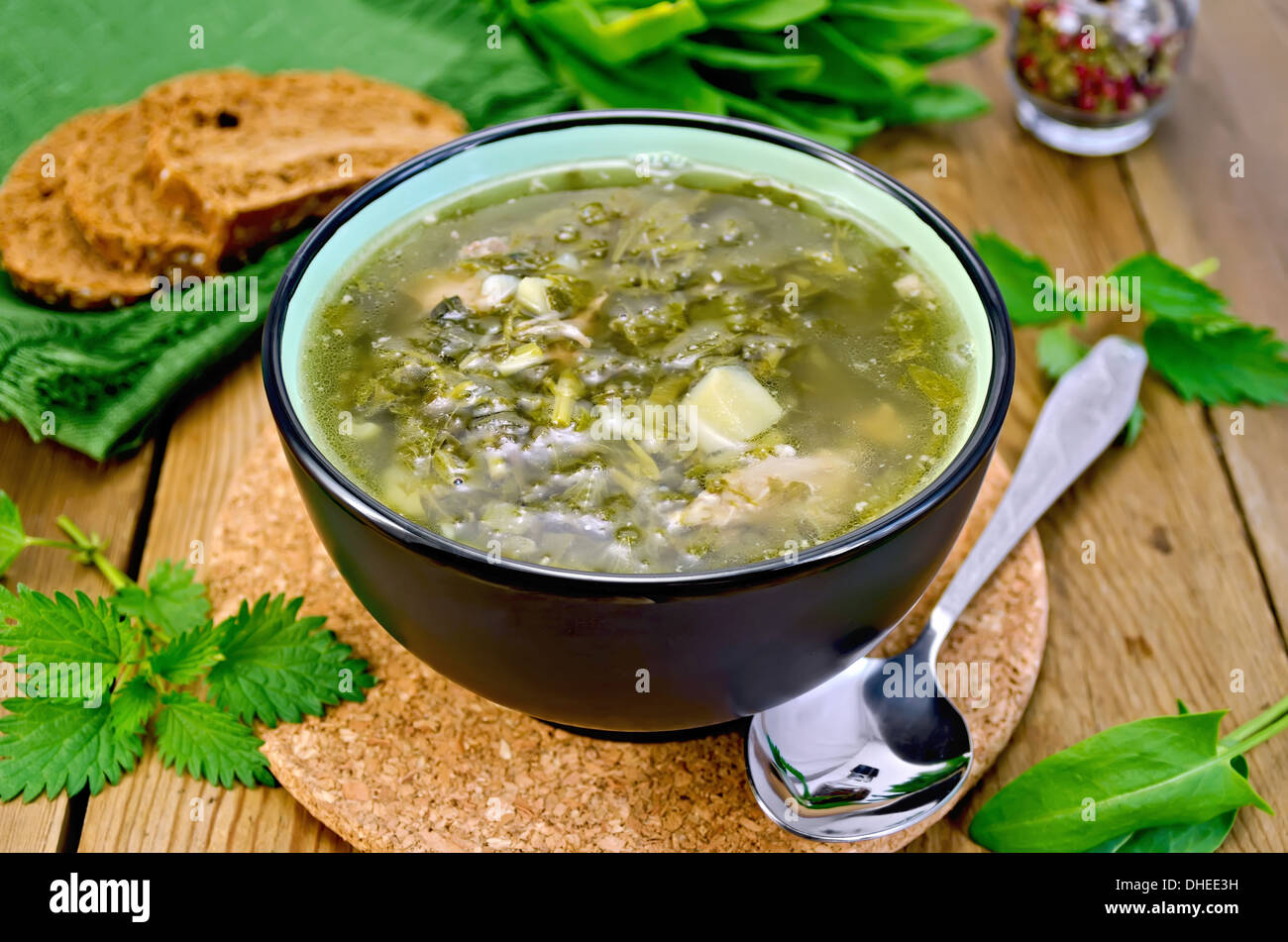 Zuppa verde di acetosella, ortica e spinaci in una ciotola, cucchiaio, pane, pepe contro un pannello di legno Foto Stock