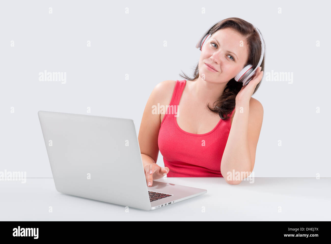 Giovane donna è in ascolto di musica attraverso le cuffie Bluetooth dal computer portatile e guardando la telecamera Foto Stock