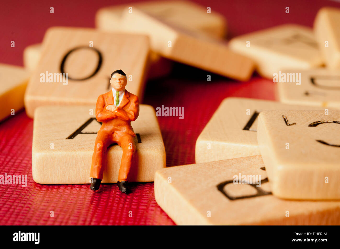 Figurina uomo seduto sulla lettera di scrabble Foto Stock