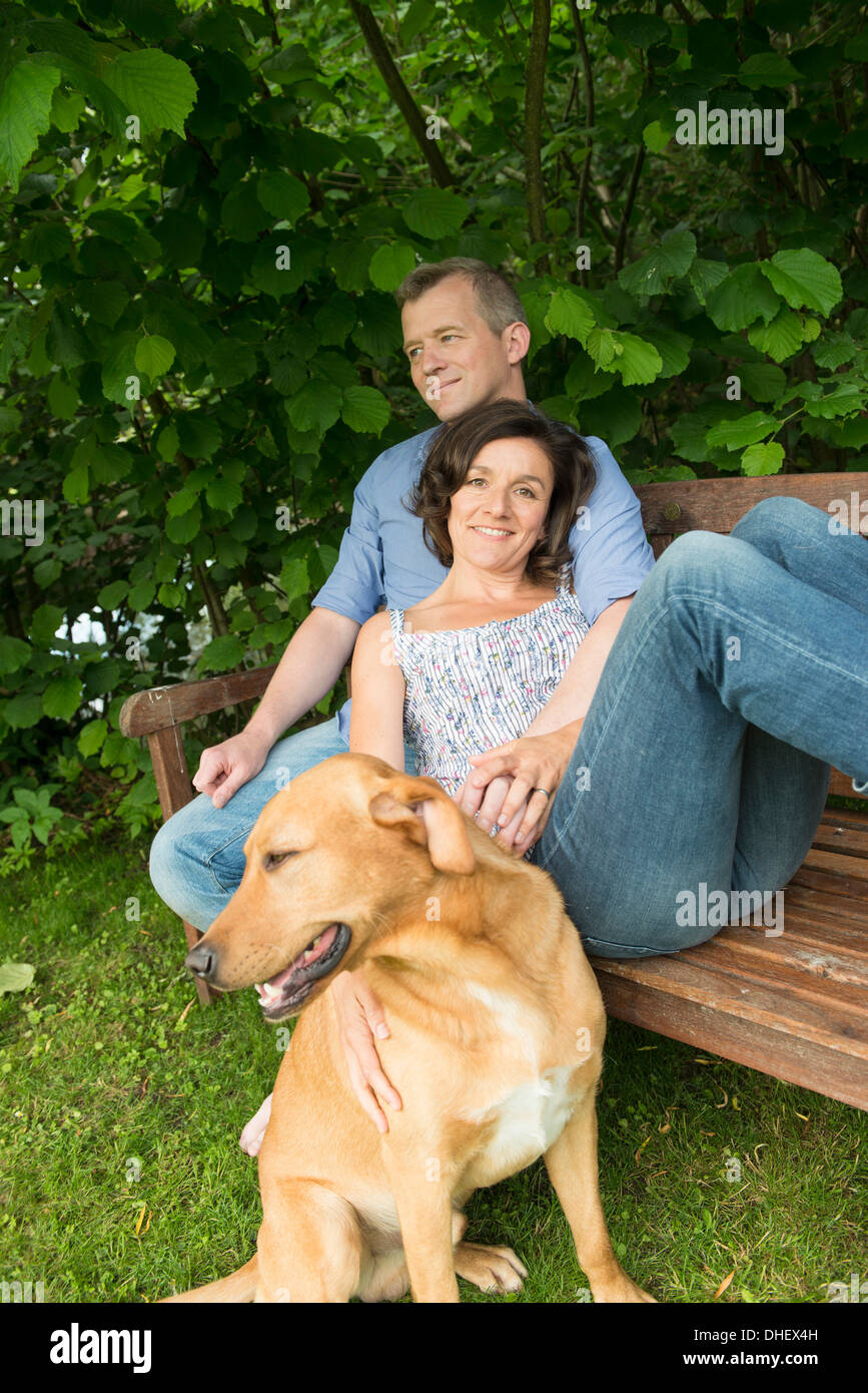 Coppia matura sedersi sulla panchina da giardino con il cane Foto Stock