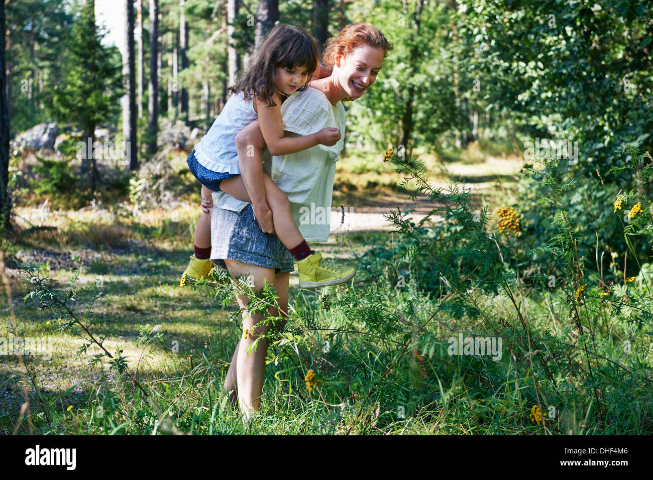 Madre dando figlia piggy back attraverso la foresta Foto Stock