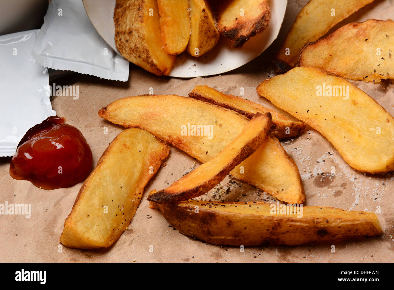 Primo piano di alcune Patatine versato su una borsa marrone. Ketchup ciuffo e pacchetti con il sale e il pepe. Foto Stock
