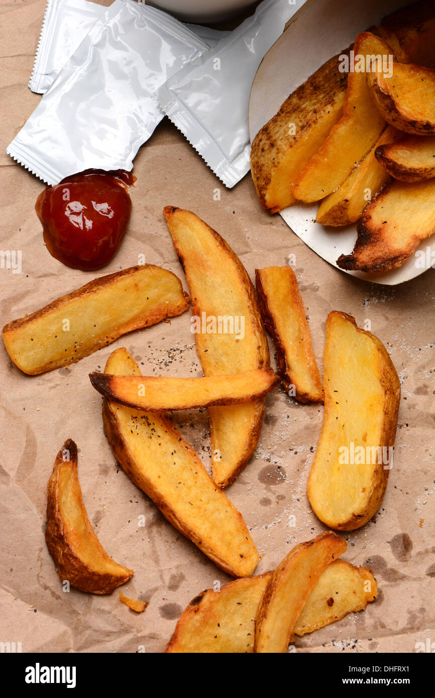 Patate Fritte versato su una borsa marrone. Ketchup ciuffo e pacchetti con il sale e il pepe. Formato verticale di riempimento del telaio. Foto Stock