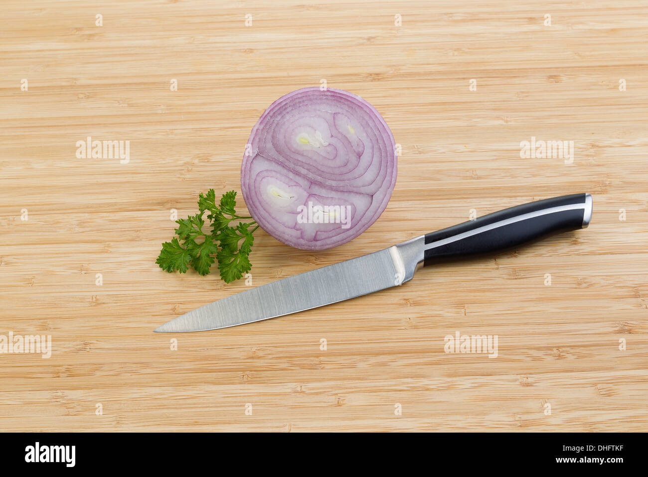 Foto orizzontale di fettine di cipolla viola e piccolo pezzo di prezzemolo con singolo coltello giacente su di bamboo naturale tagliere Foto Stock