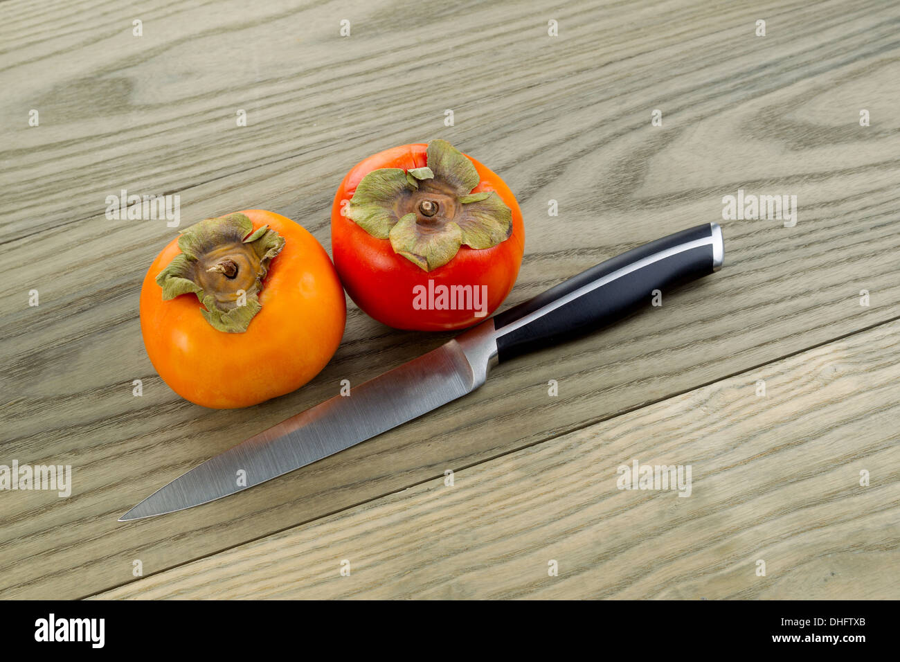 Foto orizzontale di secco fresche Cachi con singolo coltello giacente sul bianco invecchiato ceneri di pannelli di legno Foto Stock