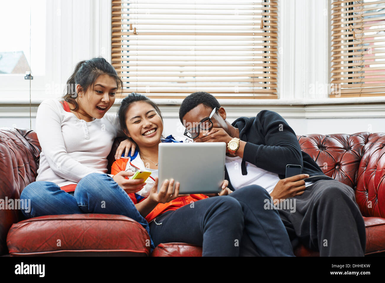 Tre giovani adulti seduti sul divano a ridere a tavoletta digitale Foto Stock