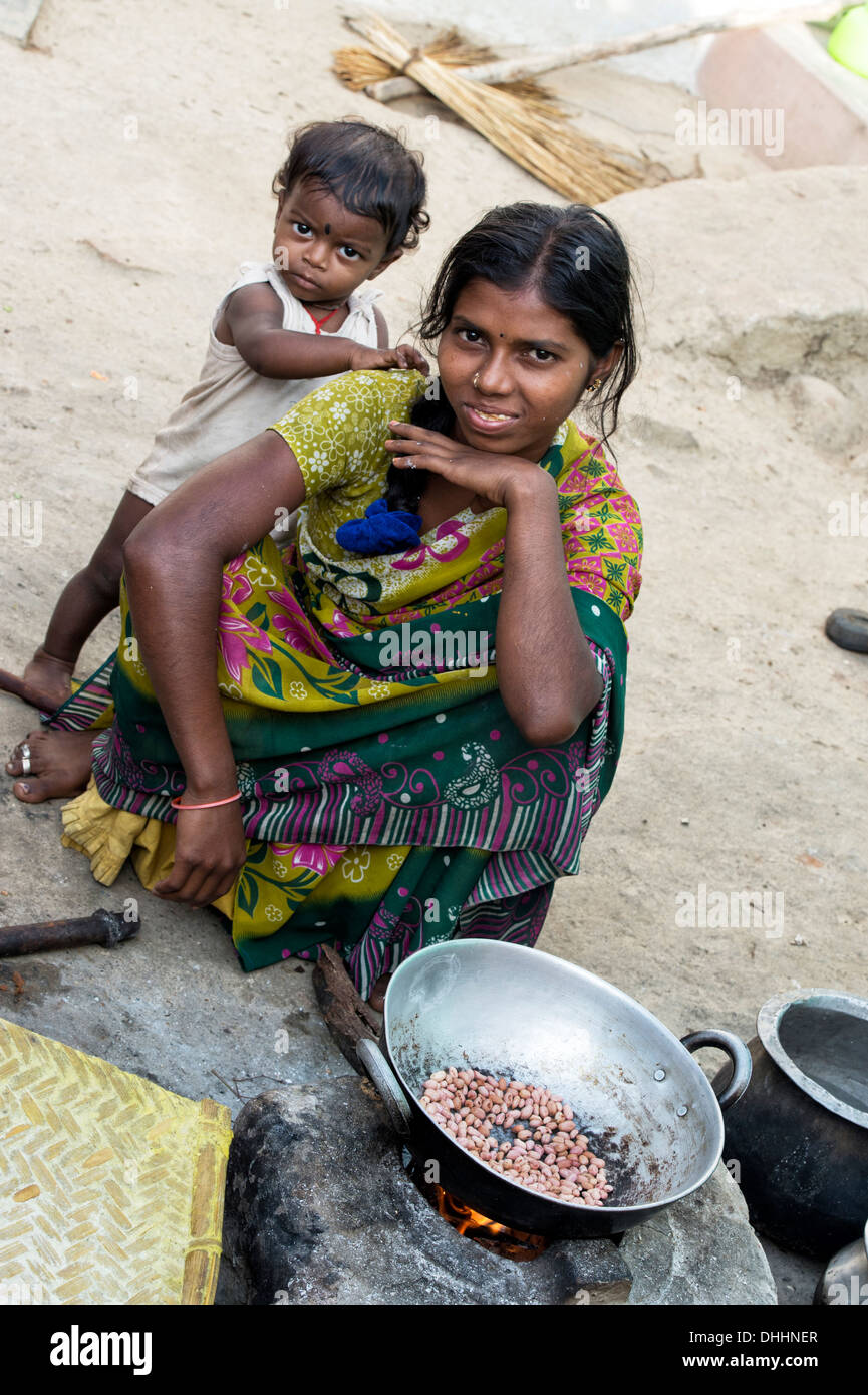 Indian ragazza adolescente e bambino di arachidi di cottura su un fuoco aperto fuori la sua casa in un borgo rurale. Andhra Pradesh, India Foto Stock