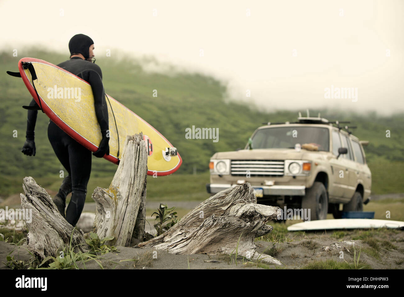 Uomo che porta la tavola da surf verso auto, Kodiak, Alaska, STATI UNITI D'AMERICA Foto Stock