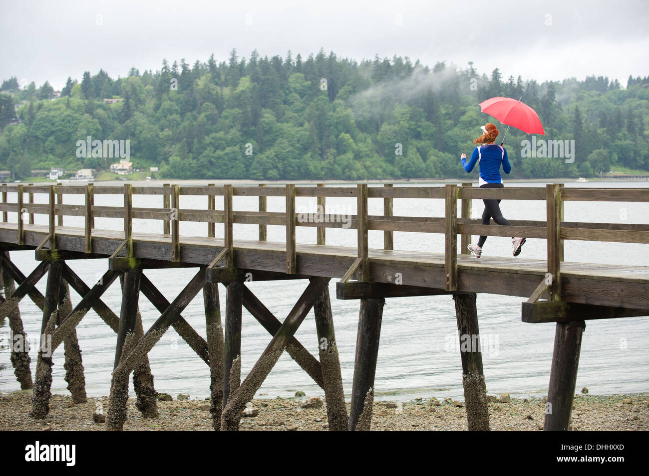Ragazza adolescente in esecuzione con ombrello sul molo, Bainbridge Island, Washington, Stati Uniti d'America Foto Stock