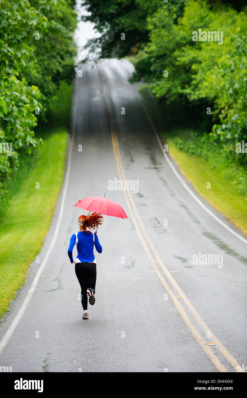 Ragazza adolescente in esecuzione con ombrellone sulla strada, Bainbridge Island, Washington, Stati Uniti d'America Foto Stock
