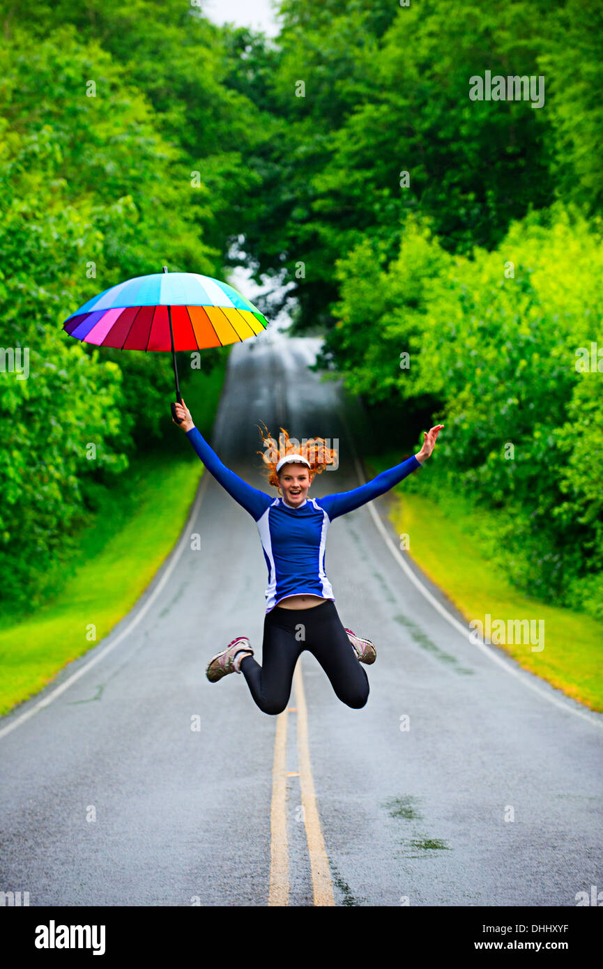 Ragazza adolescente jumping con ombrellone sulla strada, Bainbridge Island, Washington, Stati Uniti d'America Foto Stock