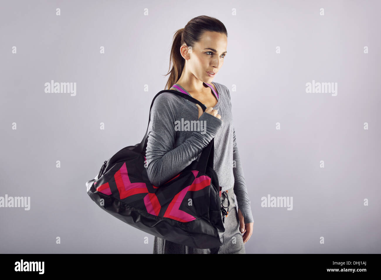 Ritratto di montare la giovane donna che trasportano borsa della palestra che guarda lontano a copyspace su sfondo grigio. Bella femmina caucasica Foto Stock