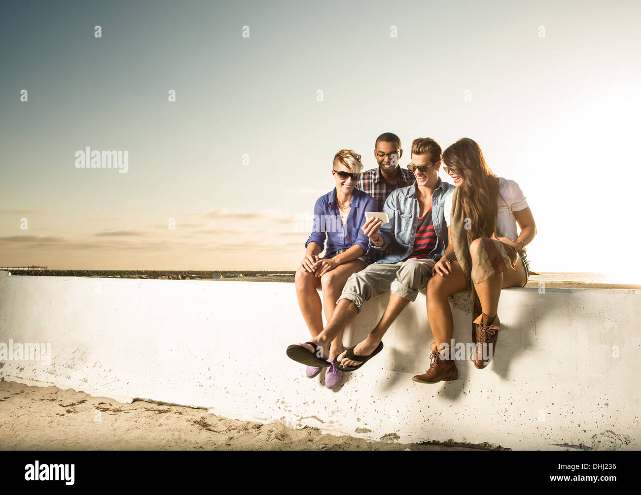 Amici seduti sulla parete con lo smartphone, Mission Beach, San Diego, California, Stati Uniti d'America Foto Stock