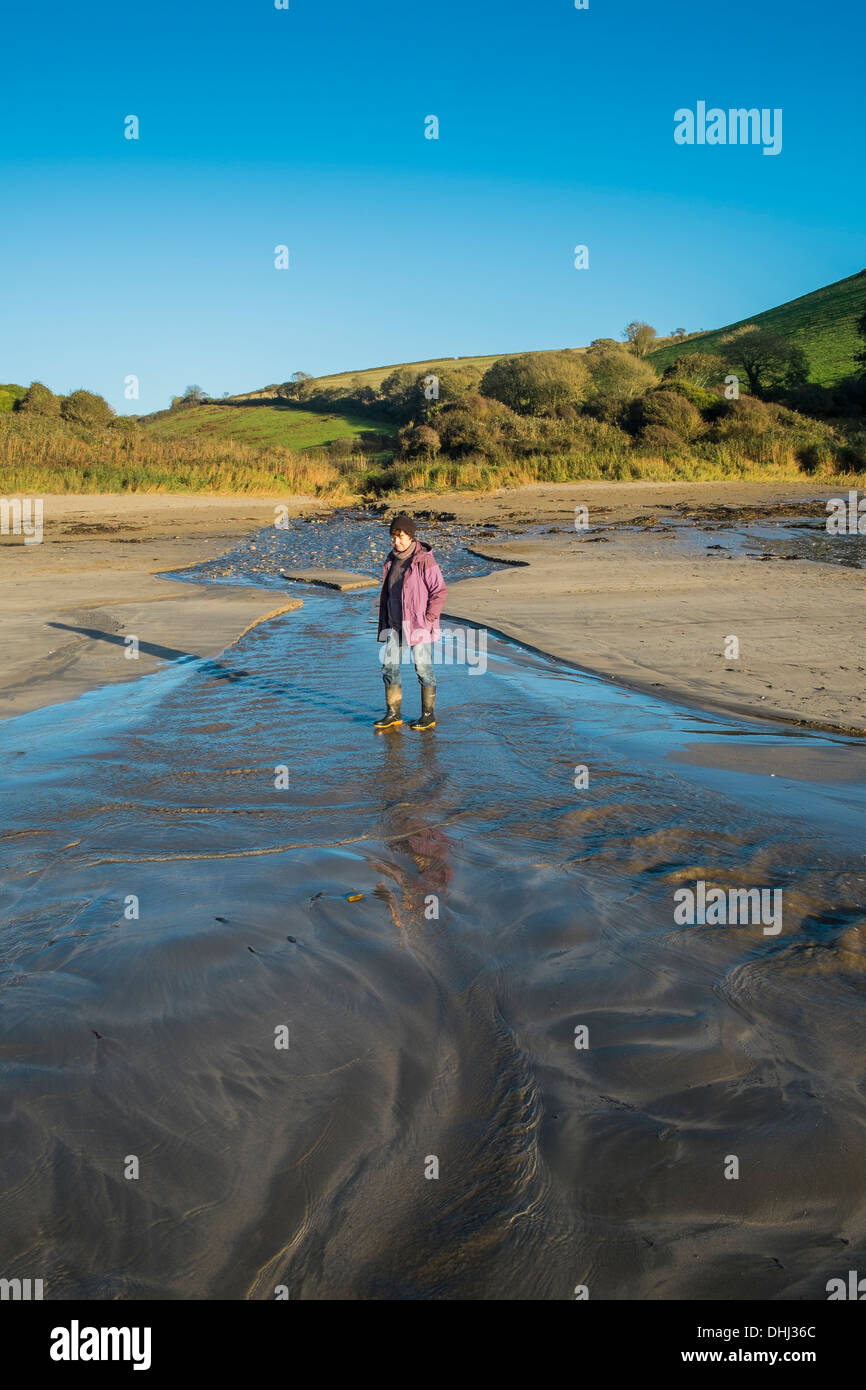 Walker attraversando un allagamento del flusso su di una spiaggia dopo piogge pesanti. Wonwell, South Devon. Regno Unito Foto Stock