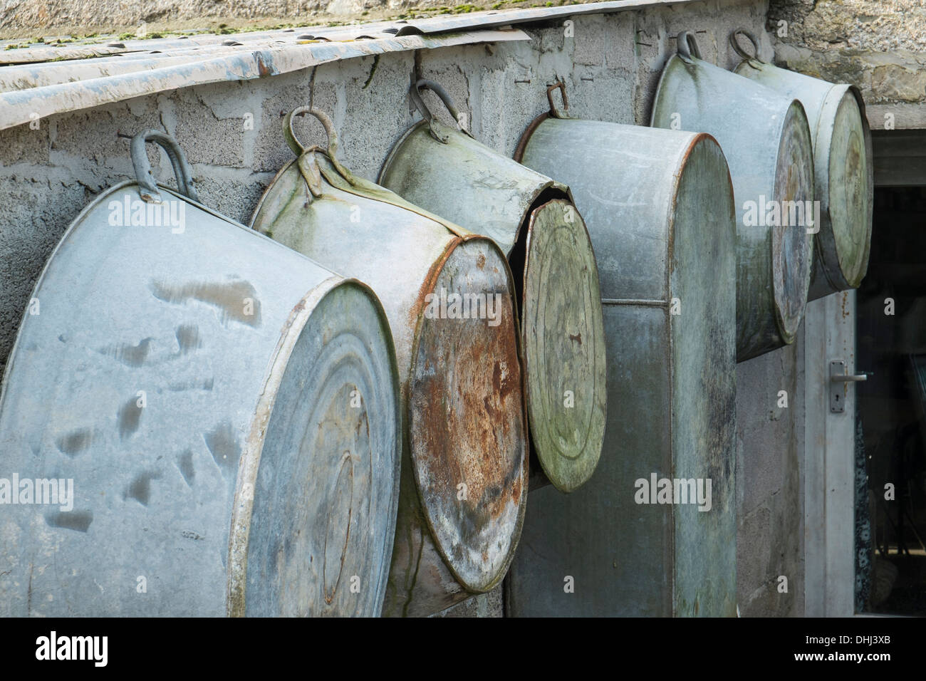 Una fila di bagni in stagno e ciotole in vecchio stile appesi su un muro di una fattoria. Modbury. Devon. REGNO UNITO Foto Stock