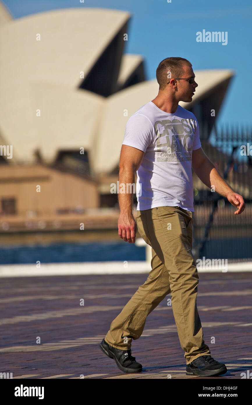 Giovane uomo cammina lungo il fronte mare di Circular Quay con la Sydney Opera House in background. Foto Stock