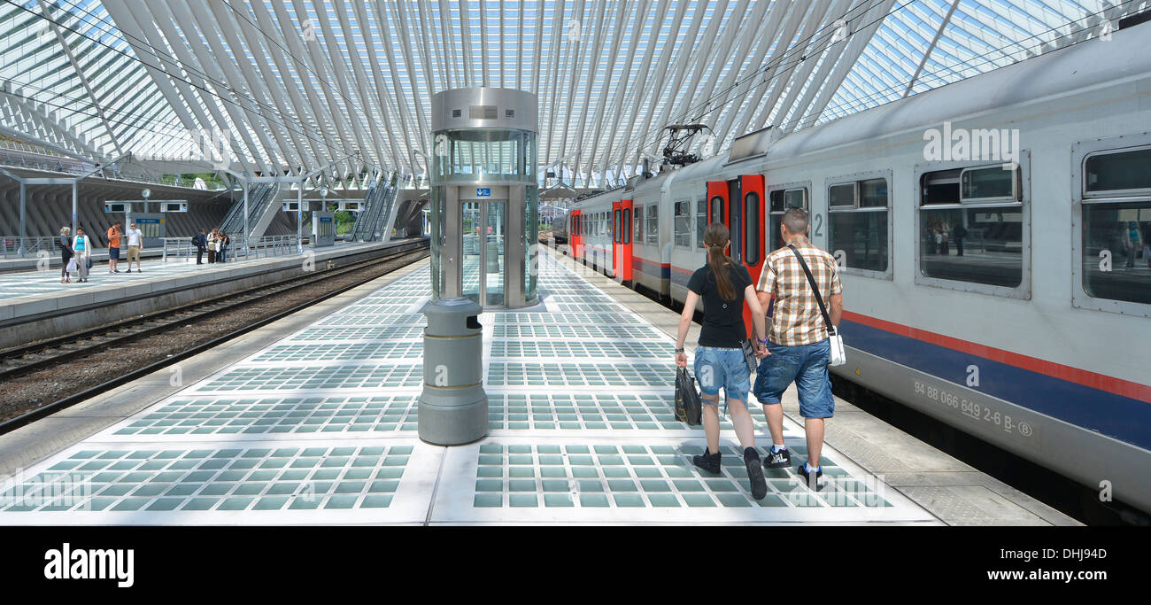 Uomo e donna giovane a piedi tenendo le mani lungo la stazione ferroviaria piattaforma Liegi in Belgio al di sotto di moderna costruzione tetto di vetro soffitto blu cielo estate giorno Foto Stock