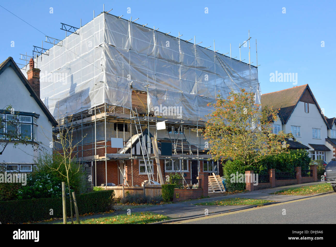 Edilizia cantiere & esistente casa indipendente in impalcatura & protezione telone di plastica durante le modifiche strutturali Essex Inghilterra UK Foto Stock