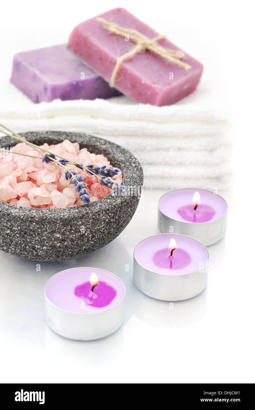 Il sale di mare in pietra ciotola con candele e saponi a base di erbe su uno sfondo bianco con la riflessione Foto Stock