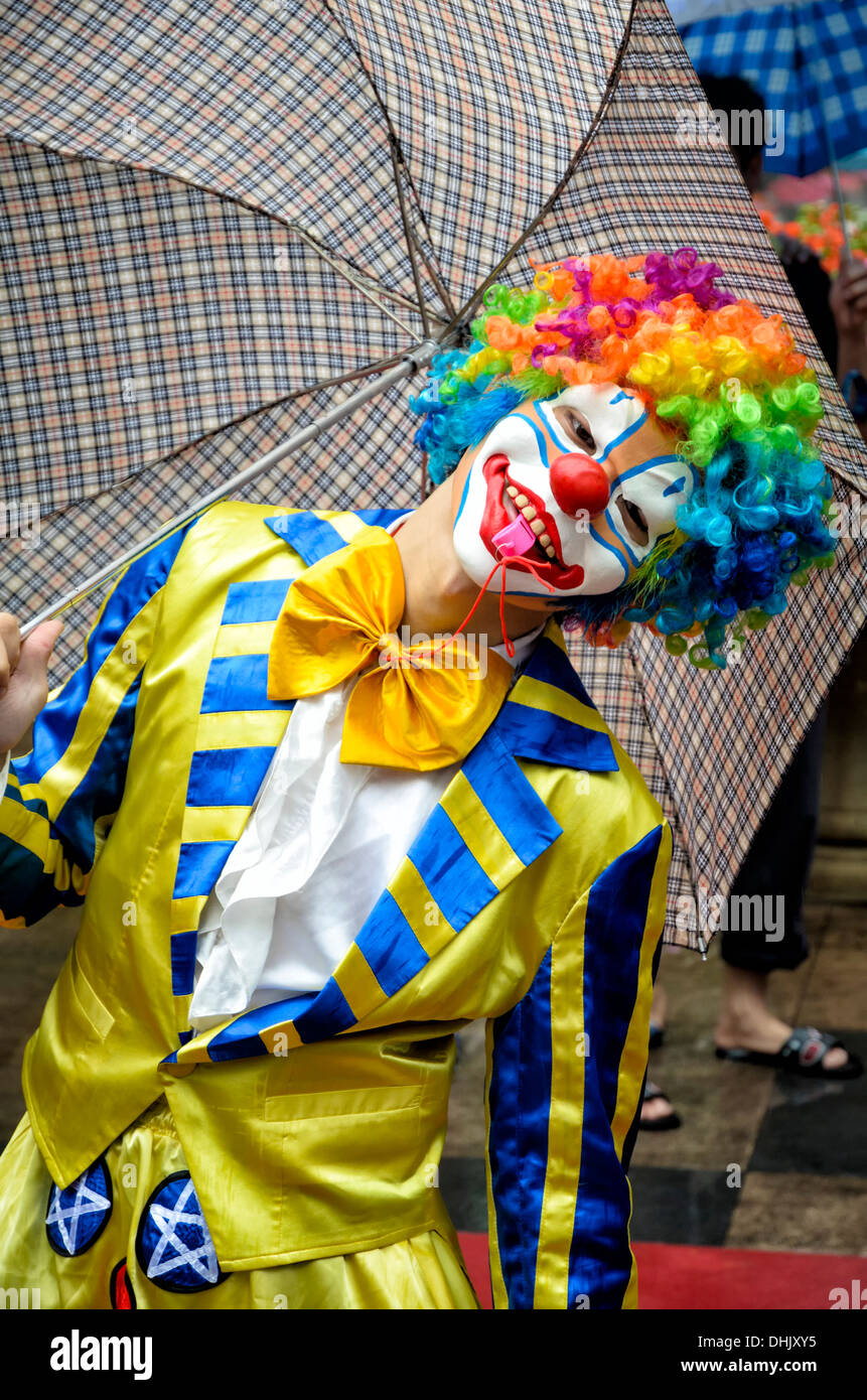 Un divertente clown in costume completo, con colorati luminosamente parrucca e maschera e giacca, soffia un fischio. Foto Stock