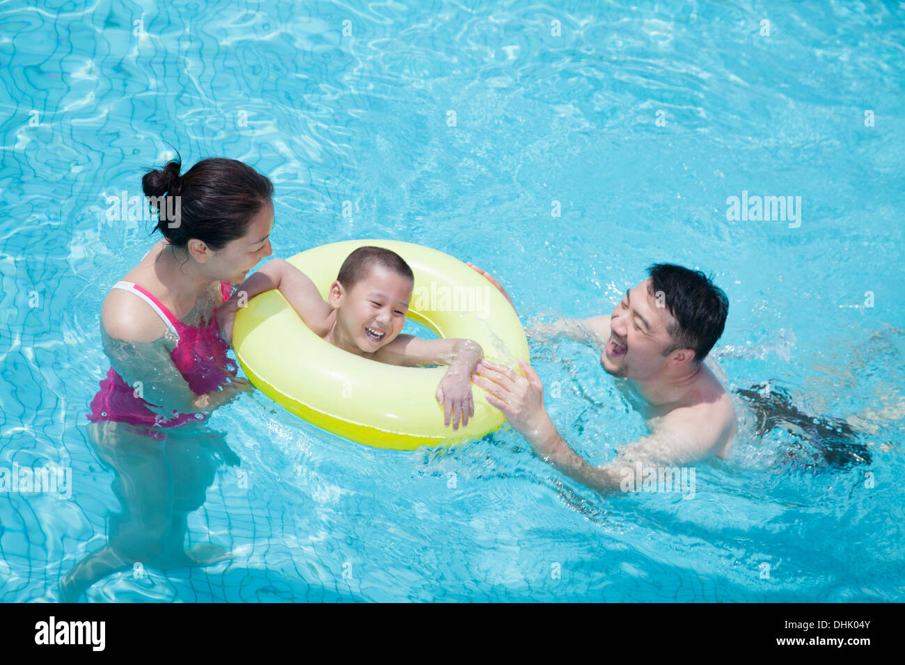 Sorridendo felice famiglia giocano nella piscina con il loro figlio in un tubo gonfiabile Foto Stock