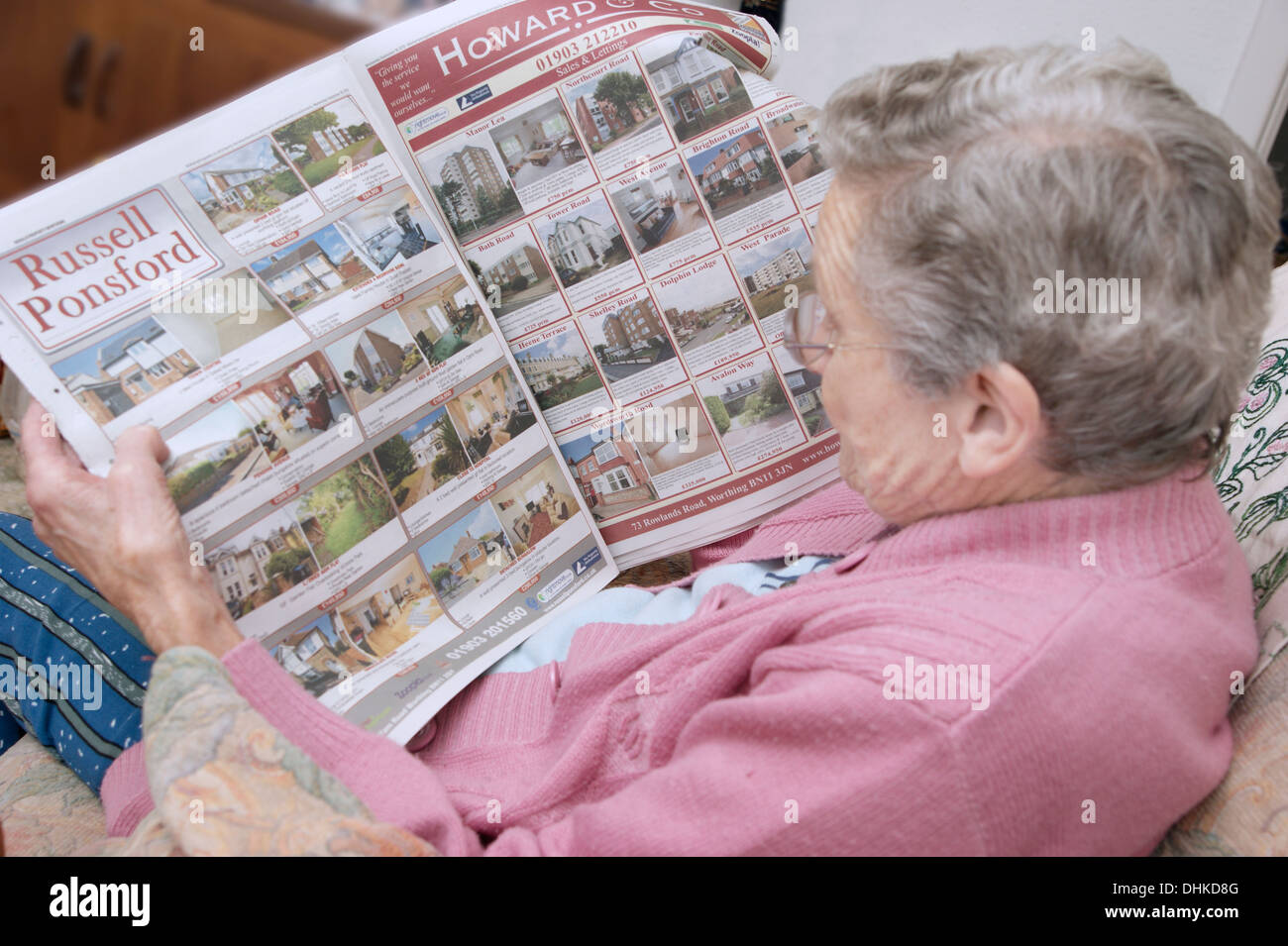 Donna anziana guardando le proprietà sulla pagine delle proprietà in un giornale locale Foto Stock
