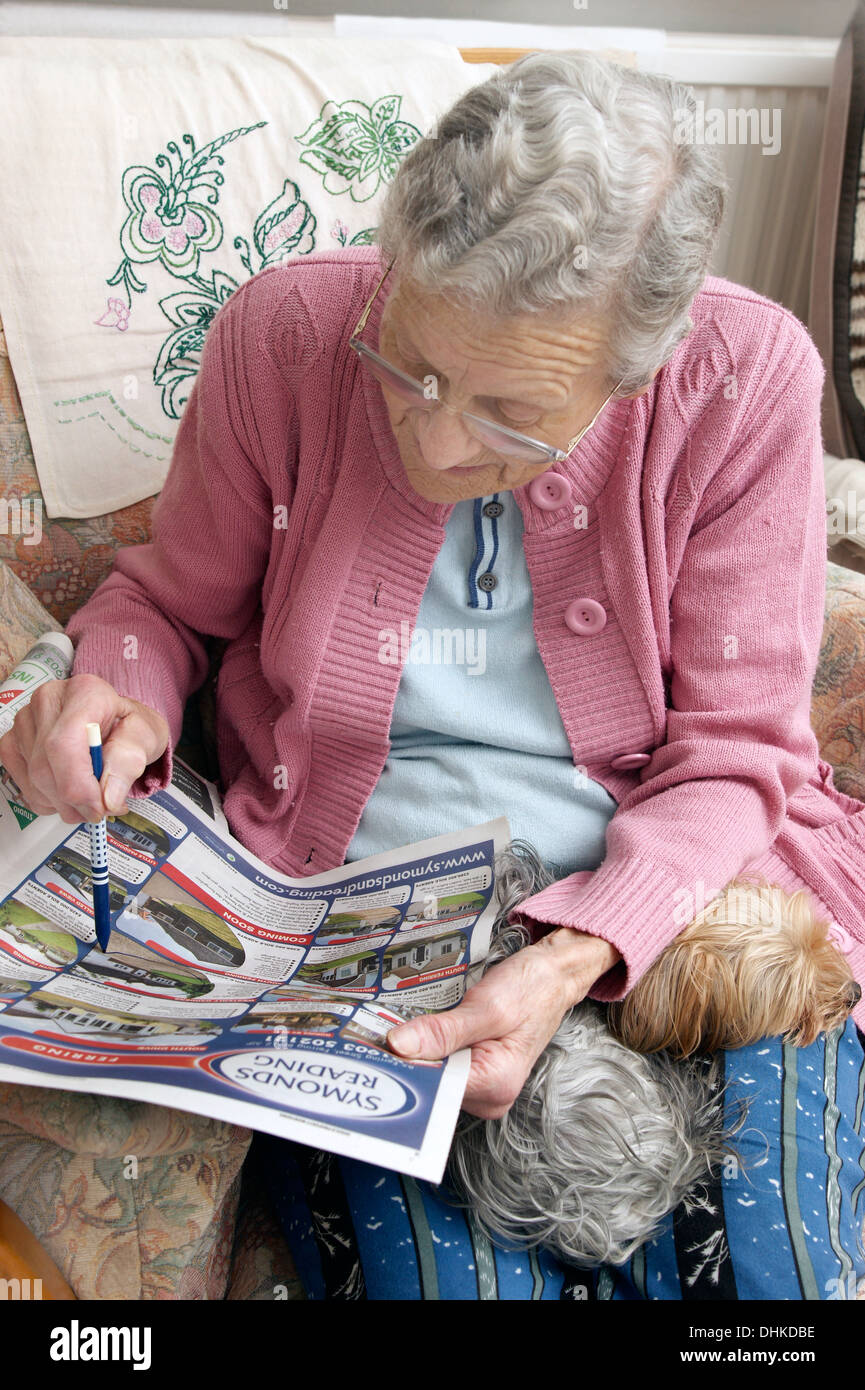 Donna anziana guardando le proprietà sulla pagine delle proprietà in un giornale locale & marcatura fuori qualcosa di interessante Foto Stock