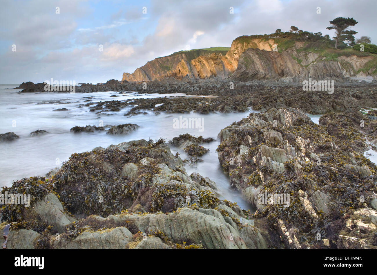 Tramonto sulle rocce a Lee Bay, North Devon, in Inghilterra con la bassa marea che mostra le frastagliate rocce sotto il mare. Foto Stock