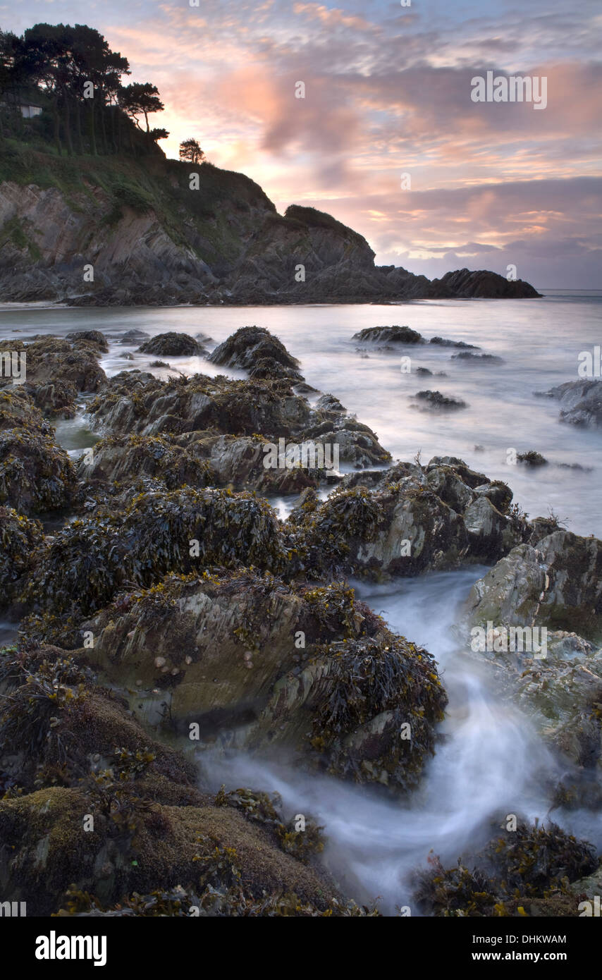 Acqua vorticoso attorno alla frastagliata jocks come la marea avanza a Lee Bay, Devon, Inghilterra come il sole tramonta in background Foto Stock