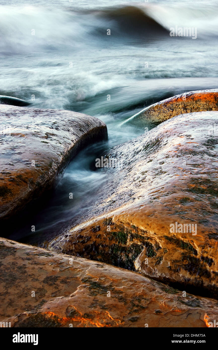 Marroncina curva pietre e mare ondeggiante. Le rocce sono bagnati e lucenti. Foto Stock