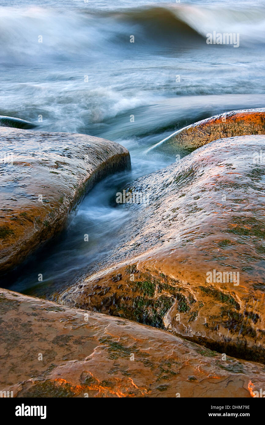 Marroncina curva pietre e mare ondeggiante. Le rocce sono bagnati e lucenti. Foto Stock
