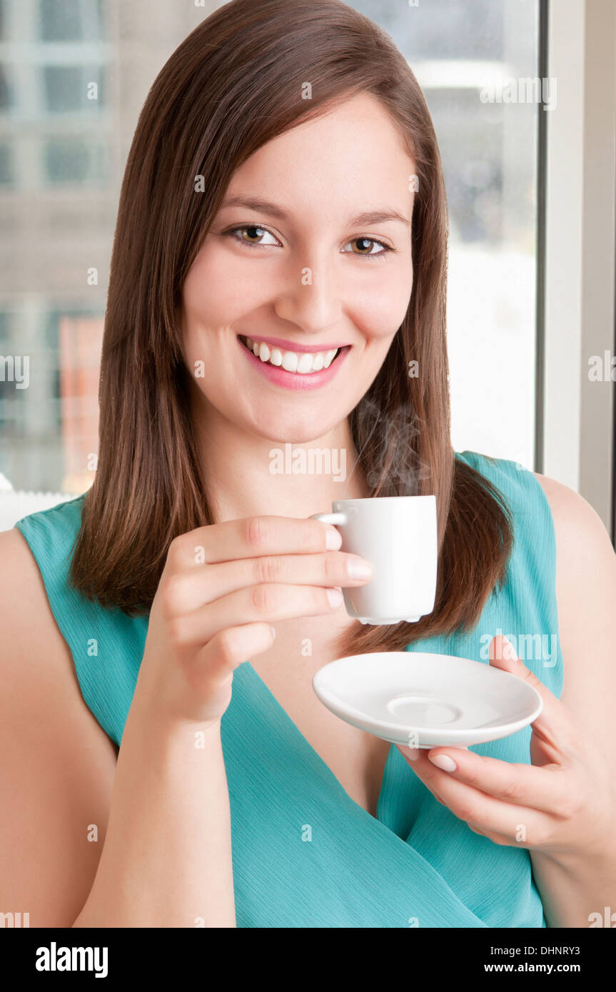 Giovane donna di bere un caffè caldo da una tazza bianca in un ufficio Foto Stock