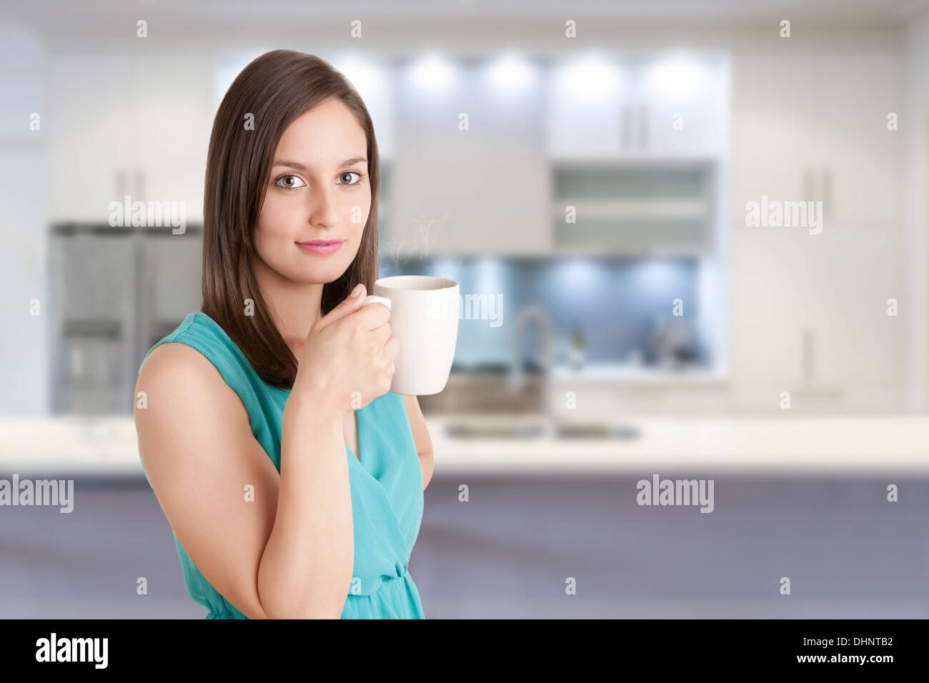 Giovane donna bere un tè caldo da una tazza bianca in una cucina Foto Stock