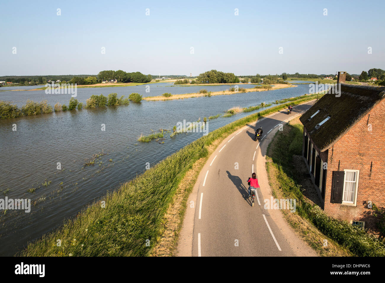 Paesi Bassi, Lienden, Donna in bicicletta e motocicli su Dyke, dove le pianure alluvionali sono allagate Foto Stock