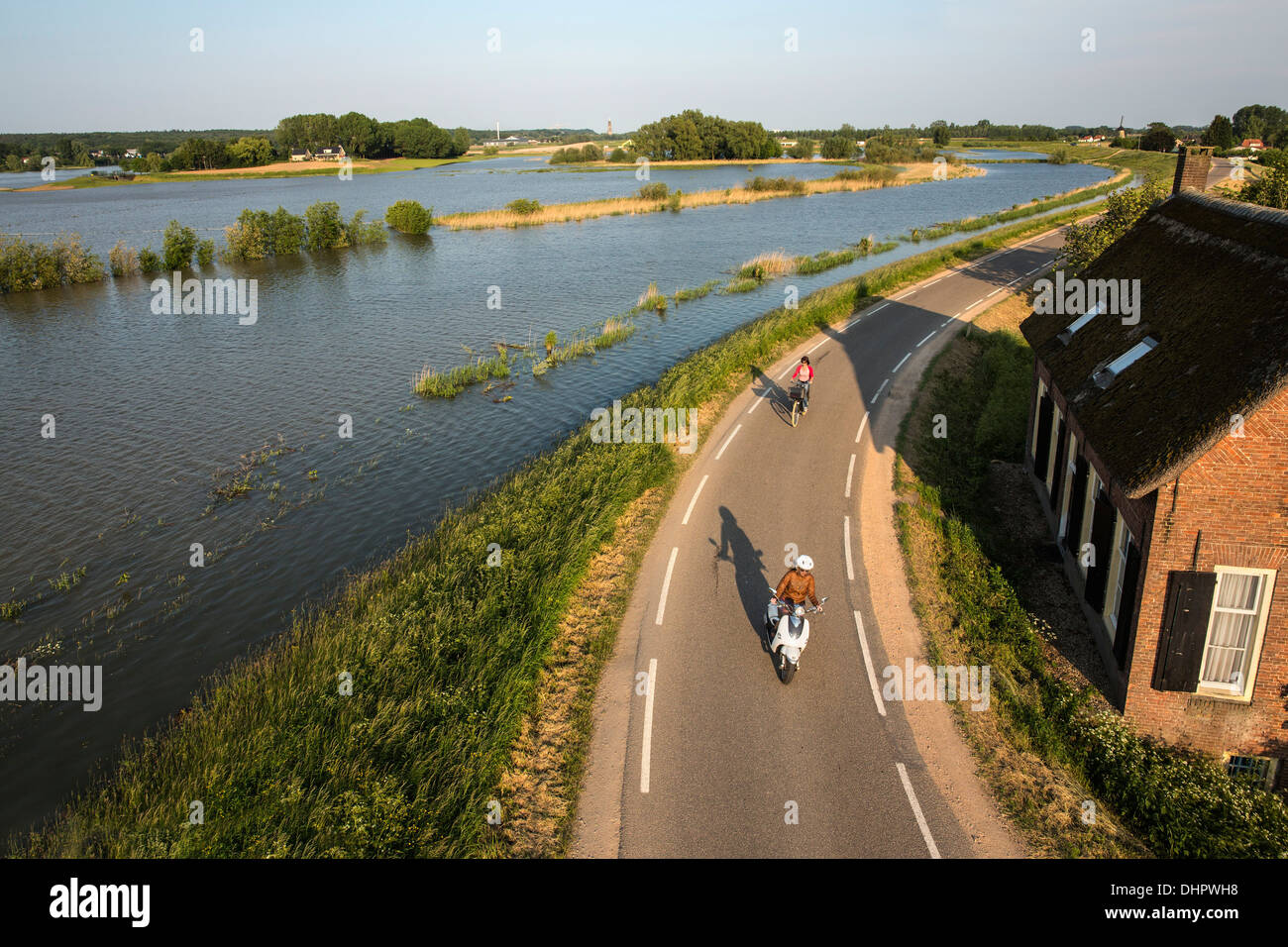 Paesi Bassi, Lienden, Donna in bicicletta e motocicli su Dyke, dove le pianure alluvionali sono allagate Foto Stock