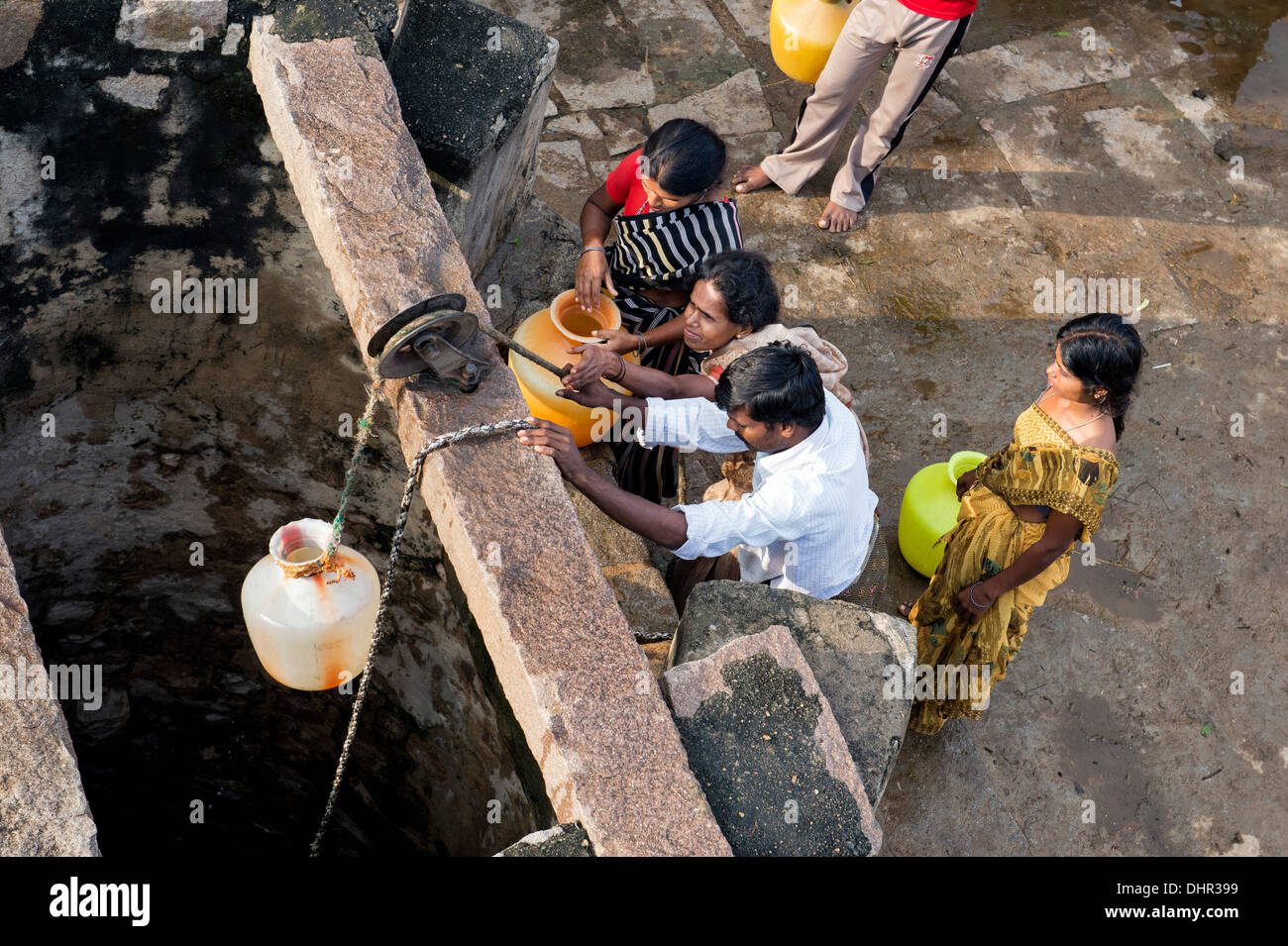 Le donne indiane e gli uomini il prelievo di acqua da un pozzo in una zona rurale villaggio indiano street. Andhra Pradesh, India Foto Stock