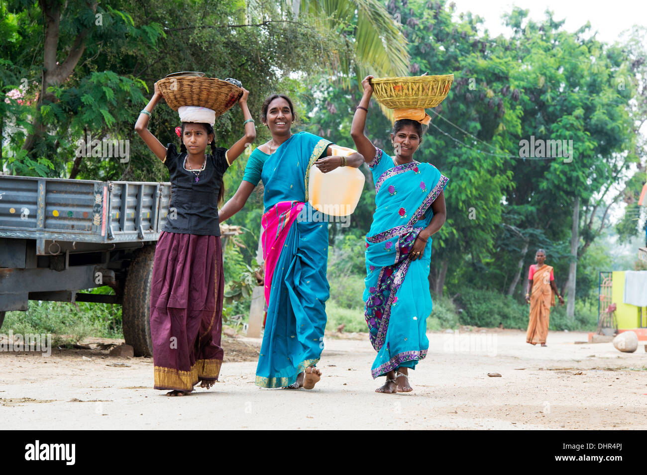 Sorridenti donne indiane e una ragazza che porta una brocca di acqua e cesti in un territorio rurale villaggio indiano street. Andhra Pradesh, India Foto Stock