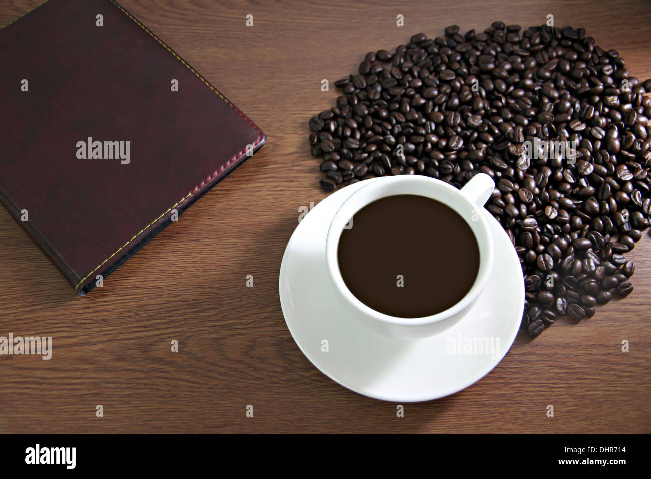 La messa a fuoco delle immagini bianco tazza di caffè e un libro sul tavolo di legno vecchio vicino i chicchi di caffè. Foto Stock