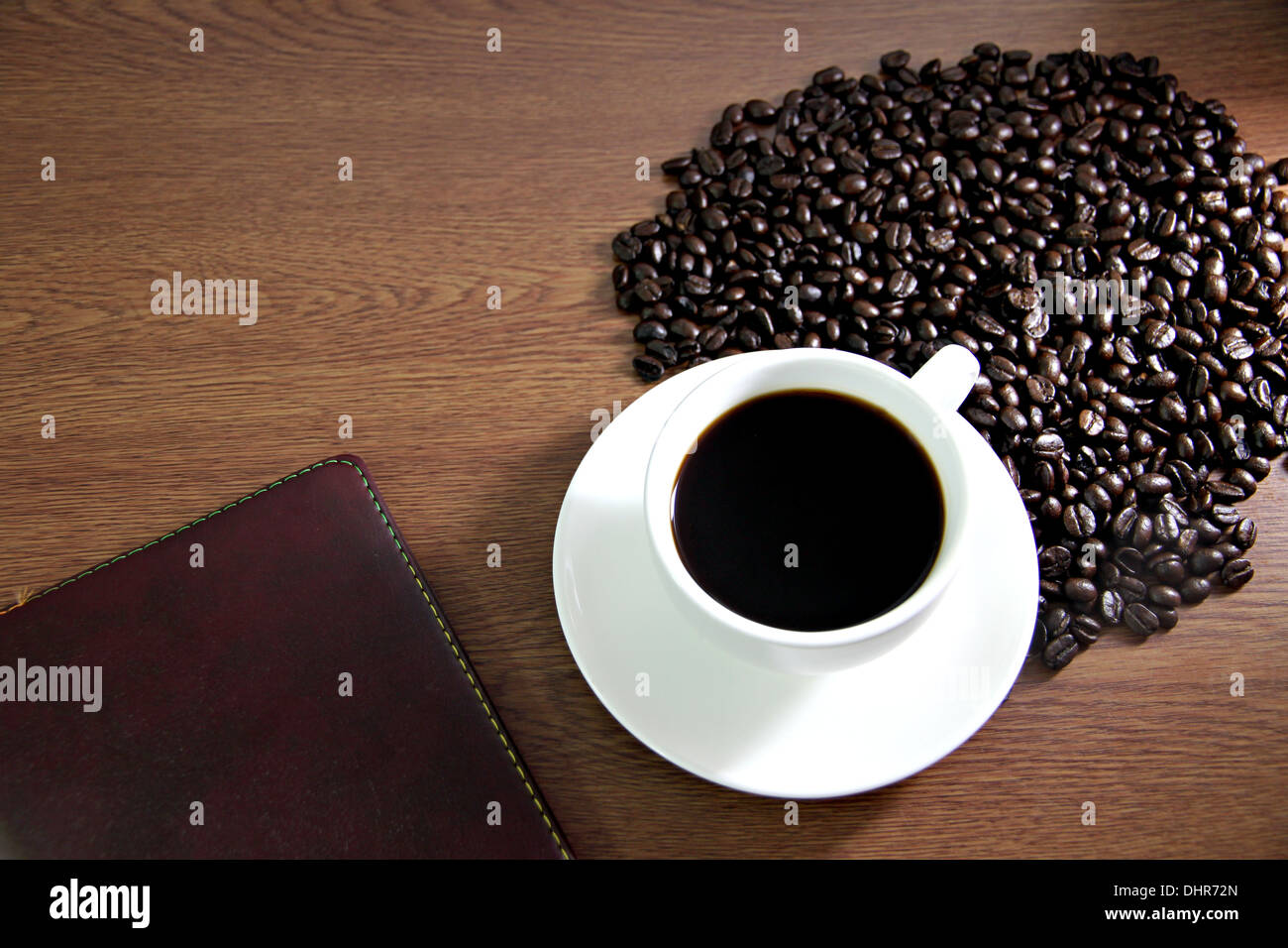 La messa a fuoco delle immagini bianco tazza di caffè e un libro sul tavolo di legno vecchio vicino i chicchi di caffè. Foto Stock