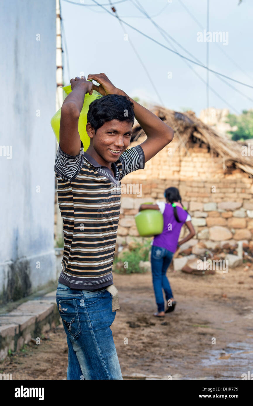 Indian ragazzo adolescente che porta una pentola di acqua lontano da un pozzo in una zona rurale villaggio indiano street. Andhra Pradesh, India Foto Stock