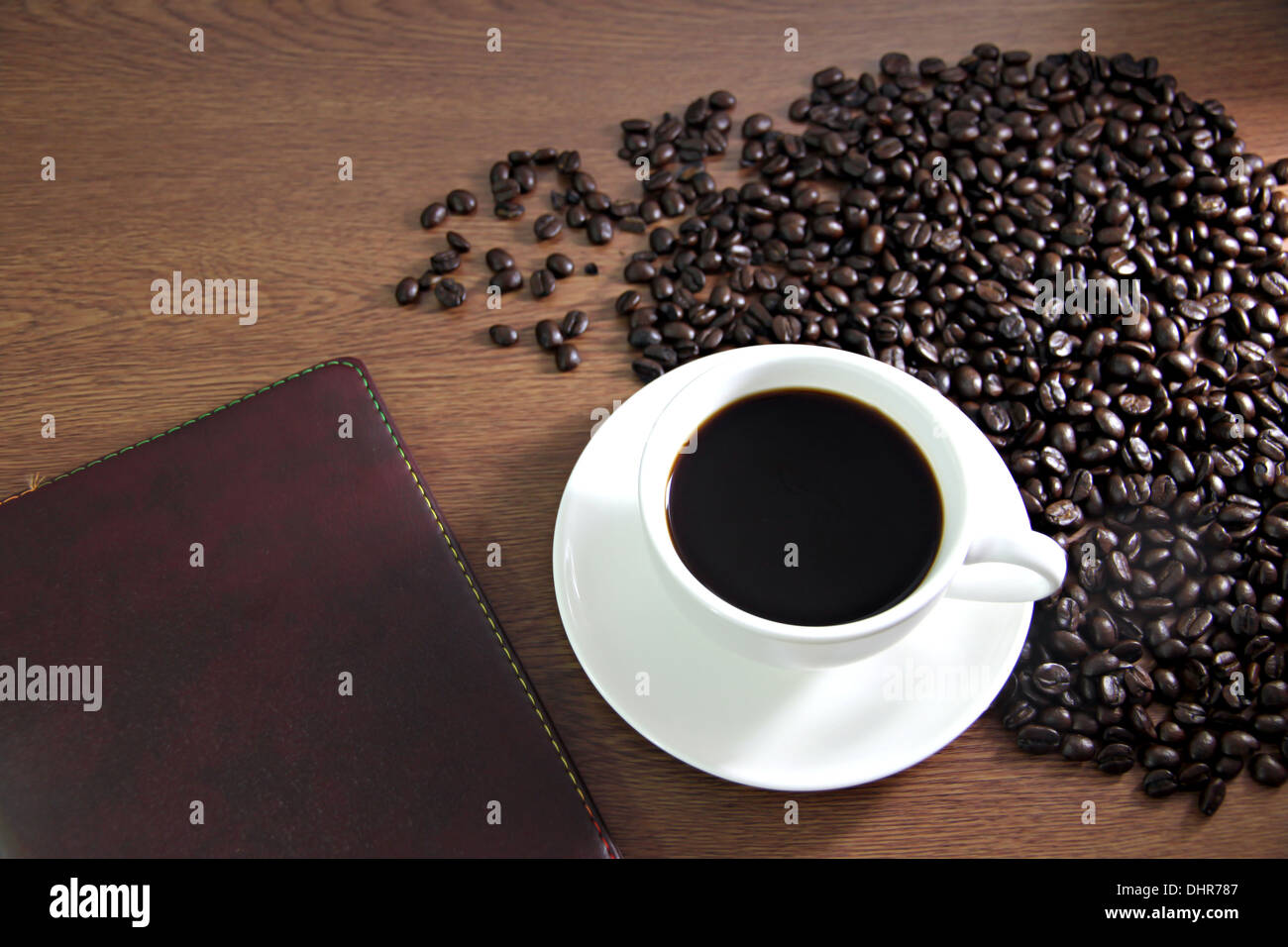 La messa a fuoco delle immagini bianco tazza di caffè e un libro sul tavolo di legno vecchio vicino i chicchi di caffè. Foto Stock