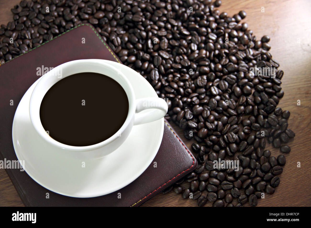 La messa a fuoco delle immagini bianco tazza di caffè e un libro sul tavolo di legno vecchio vicino i chicchi di caffè. Foto Stock