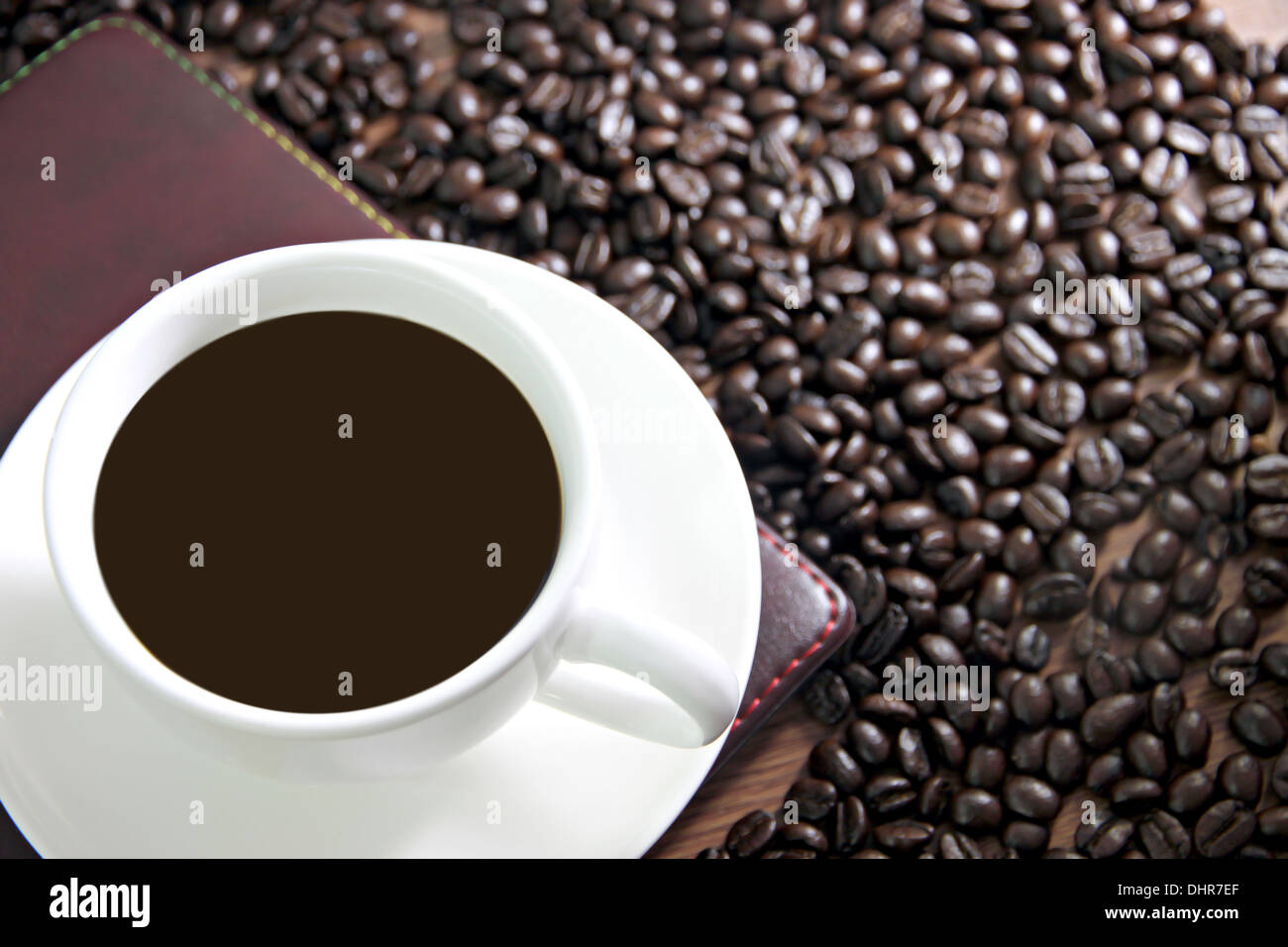 La messa a fuoco delle immagini bianco tazza di caffè e un libro sul tavolo di legno vecchio vicino i chicchi di caffè. Foto Stock