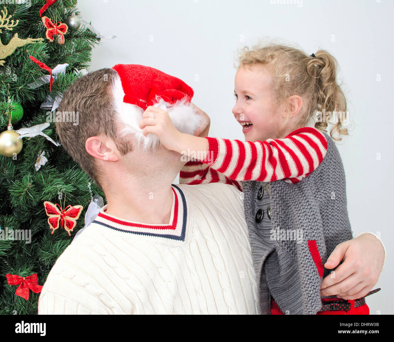 Padre e figlia divertendosi al Natale. Ragazza cercando di mettere su Santa's hat sul padre. Foto Stock