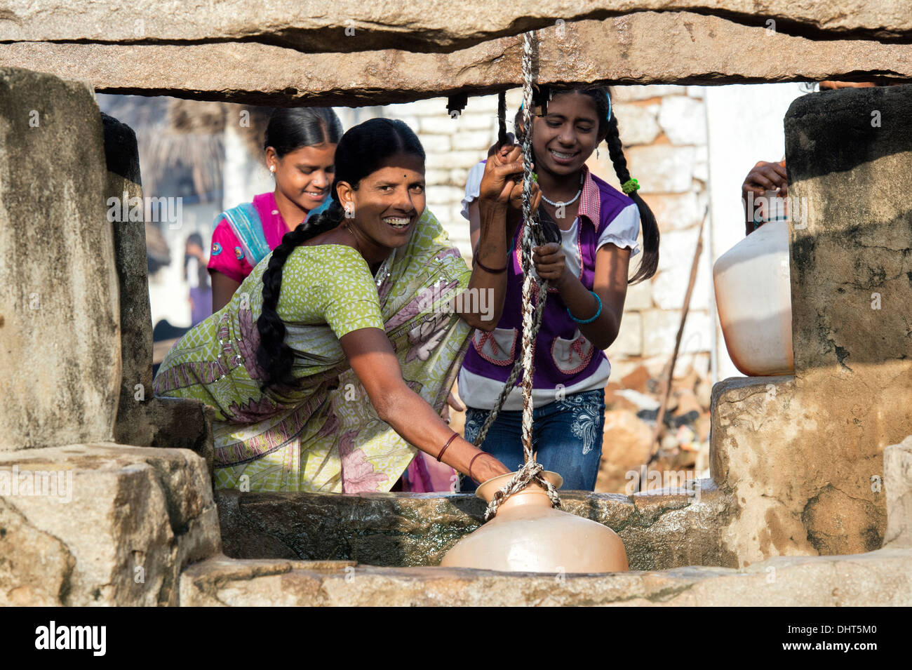 Donna indiana e ragazze adolescenti il prelievo di acqua da un pozzo in una zona rurale villaggio indiano street. Andhra Pradesh, India Foto Stock