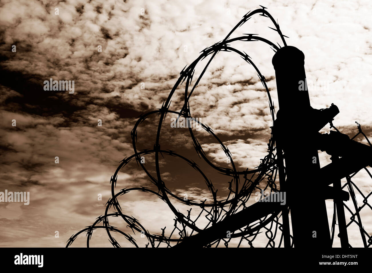 Un filo spinato prigione recinto stagliano contro un oscuro, ambra moody sky. Foto Stock